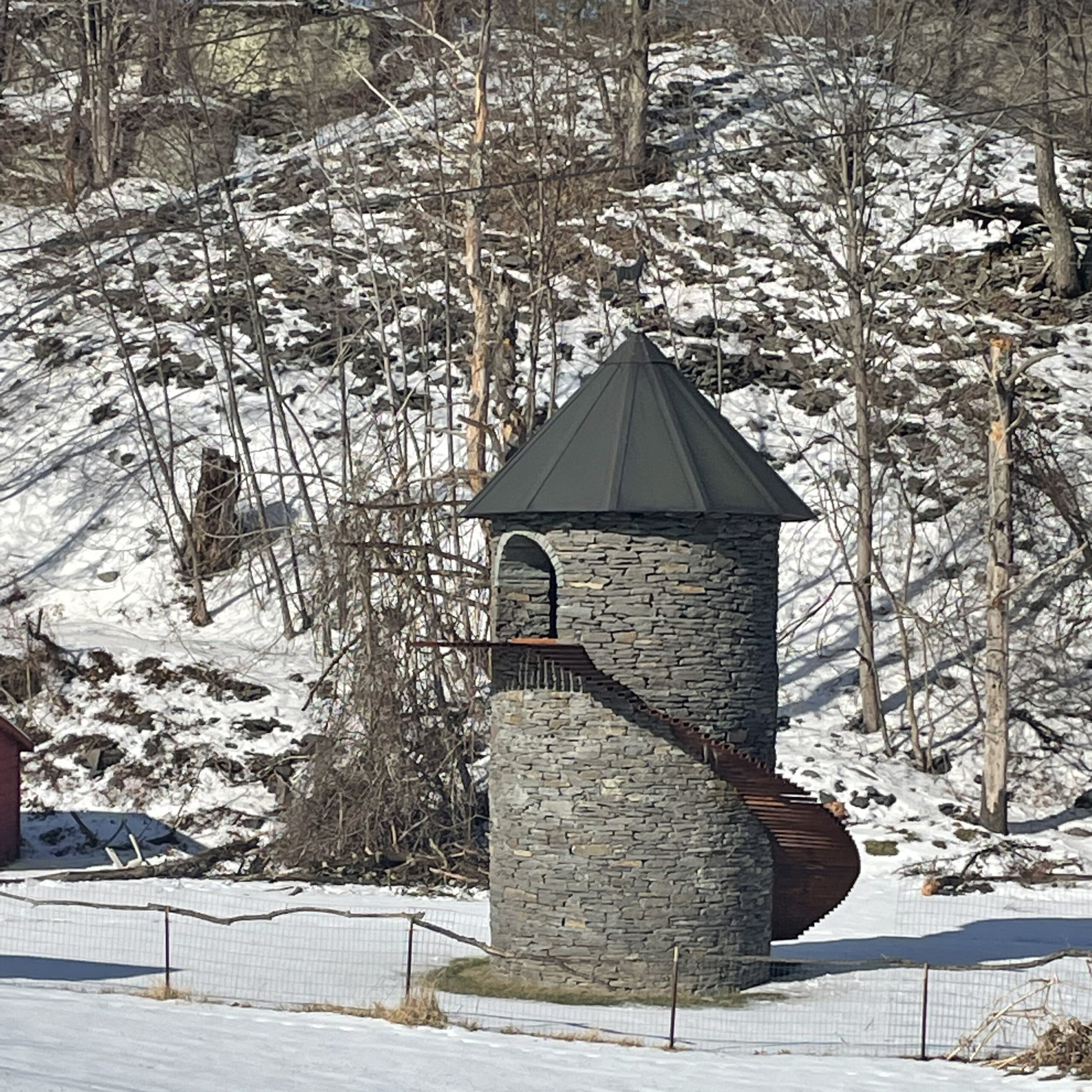 Stone tower personal temple with corten spiral ramp in a snowy wooded landscape